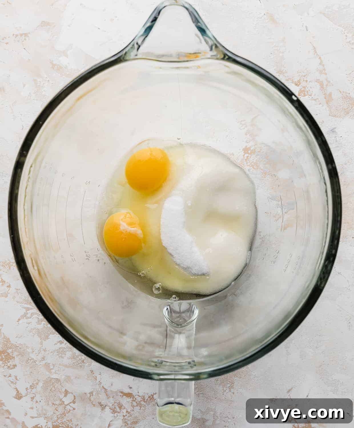 Eggs, granulated sugar, and vegetable oil in a glass stand mixer bowl before mixing, showing the distinct layers of ingredients.