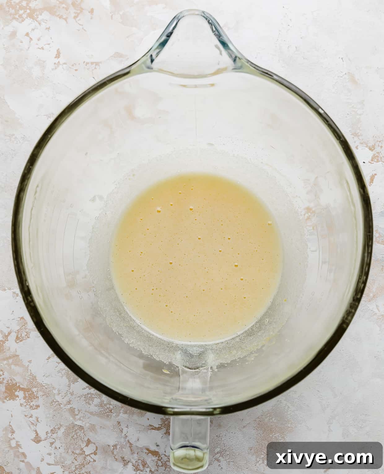 A light yellow, smooth, and creamy wet mixture of eggs, sugar, and oil in a glass mixing bowl after being beaten, ready for pumpkin and vanilla.
