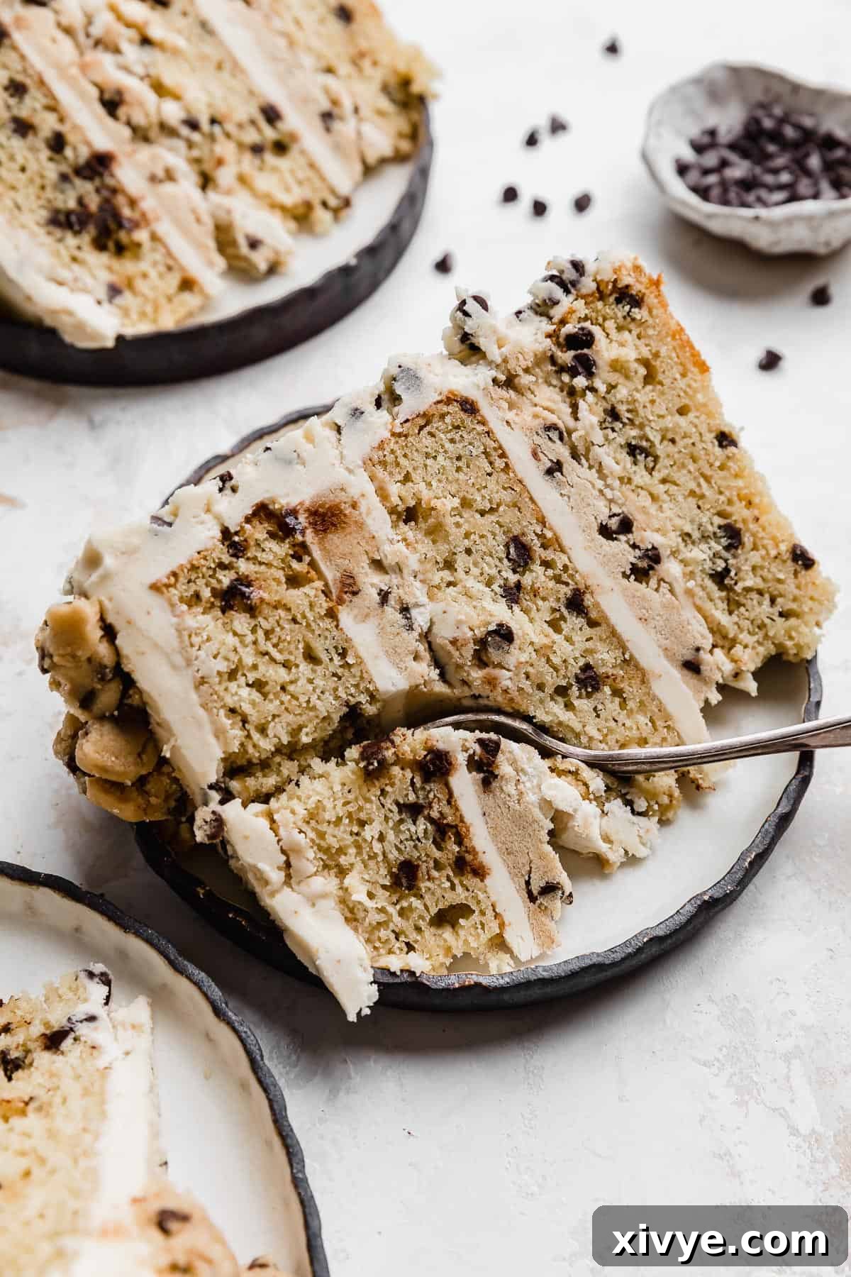 A slice of Cookie Dough Cake made with browned butter on a white plate with a fork cutting into the top of the cake slice.