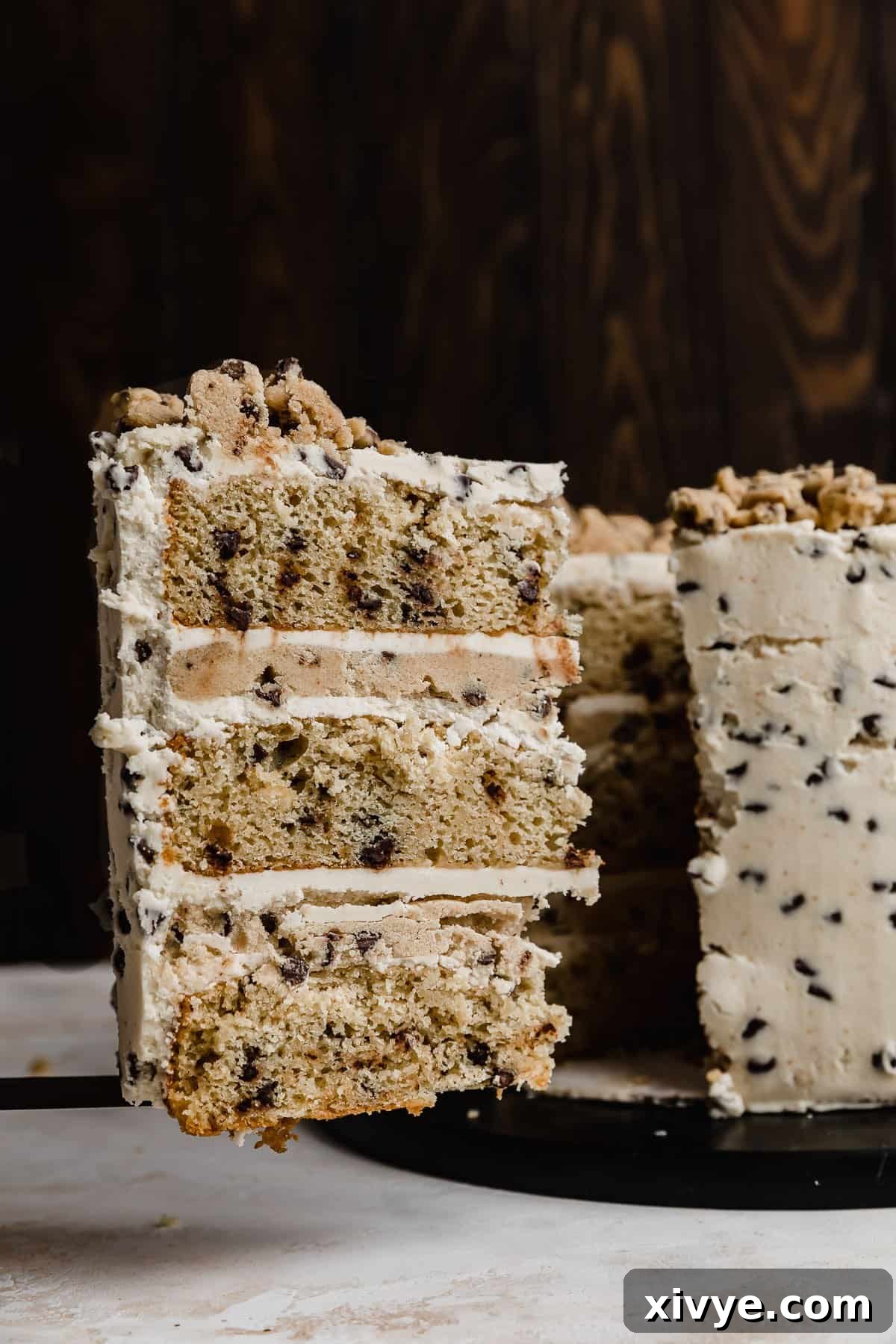 A slice of cookie dough layered cake on a serving spatula against a black background.