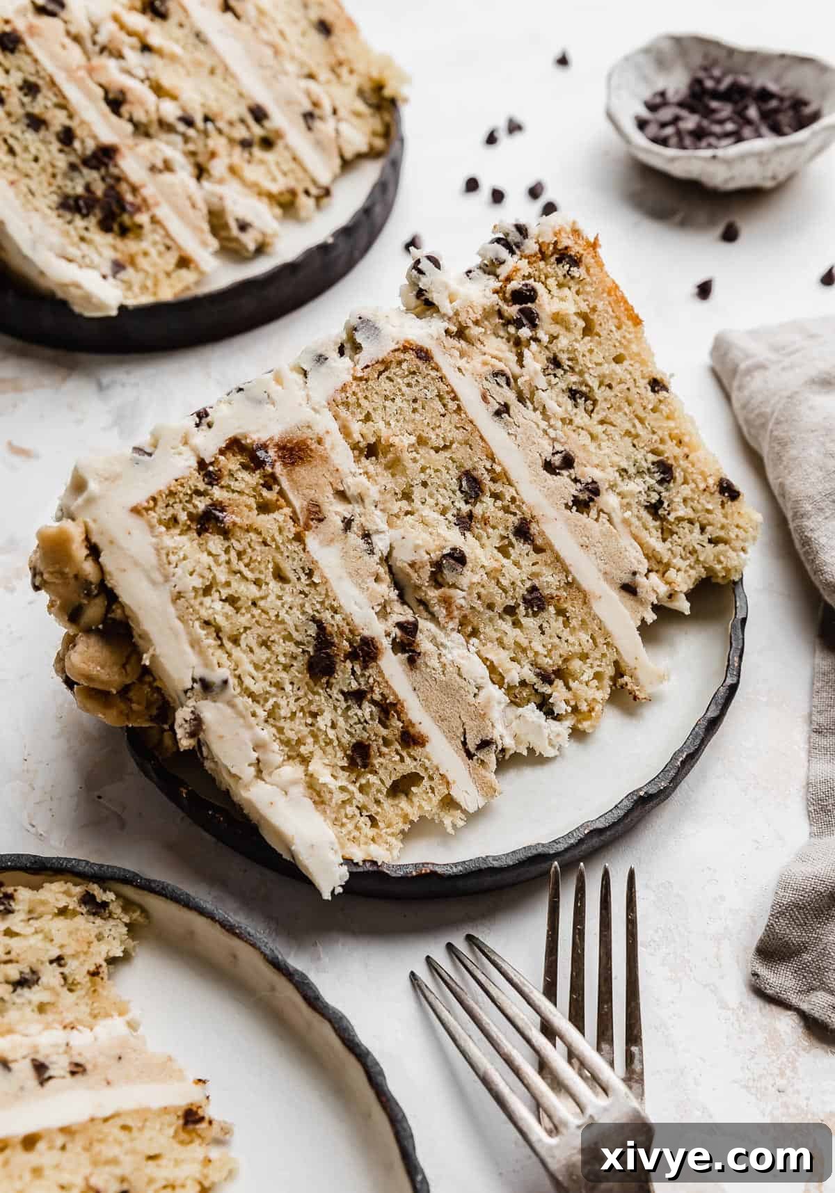 A slice of Cookie Dough Cake that has edible cookie dough between each cake layer, on a black rimmed white plate.