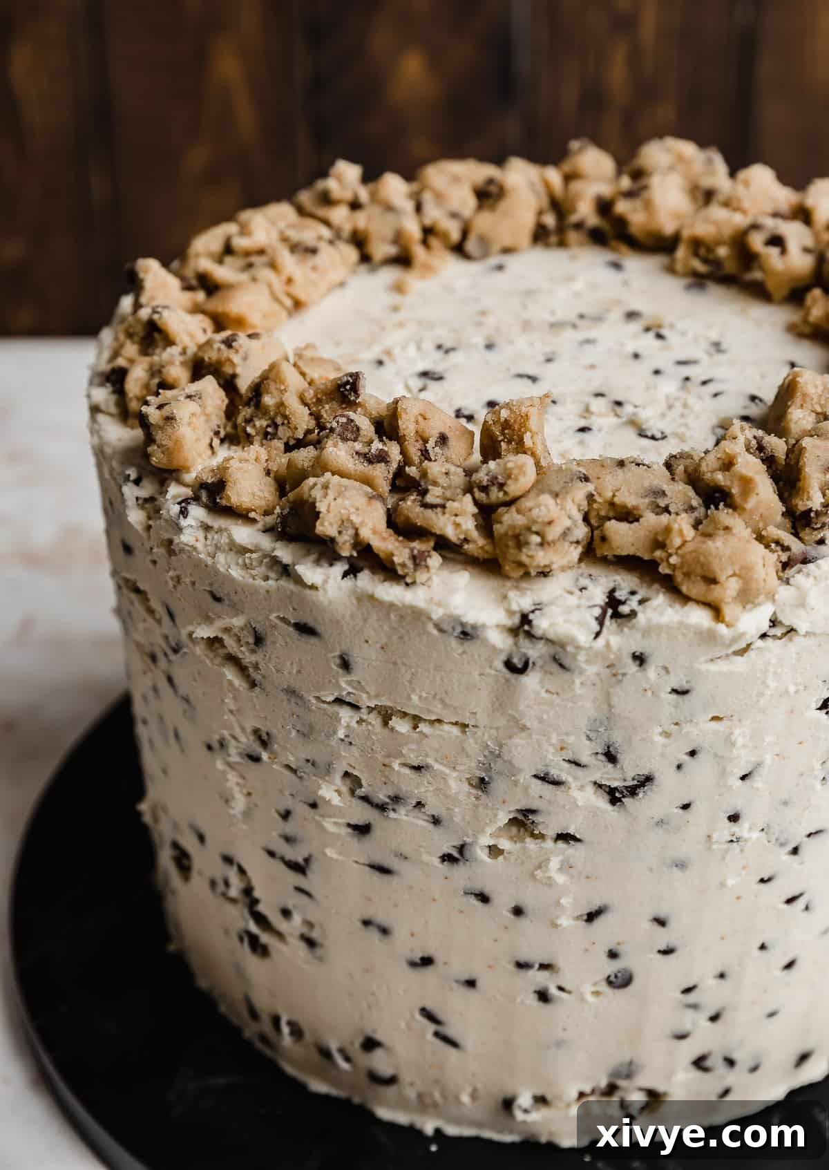A layered brown butter cookie dough cake frosted with a mini chocolate chip flour based white frosting and topped with edible cookie dough on the top of the cake.