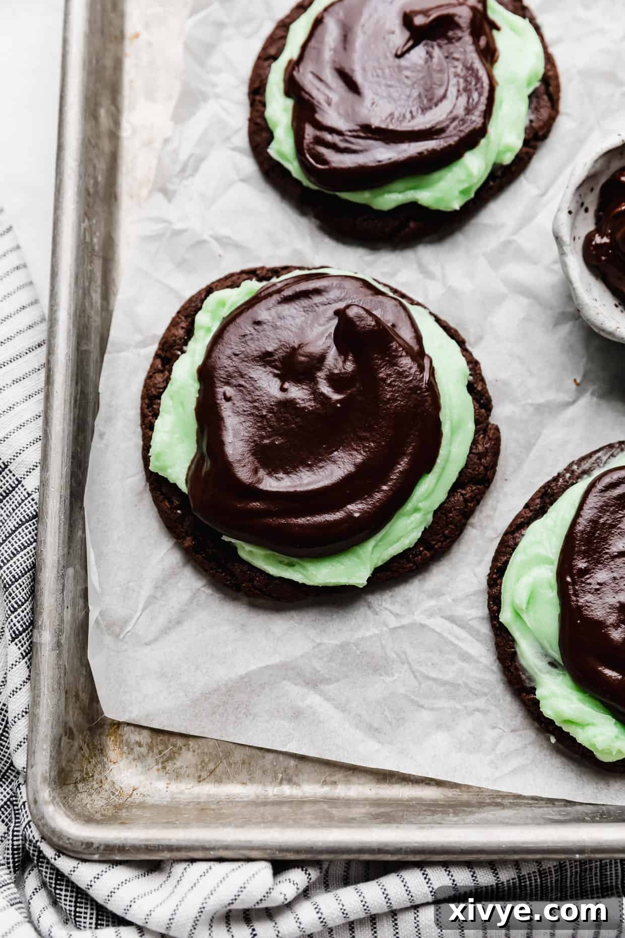 Decadent Mint Brownie Cookie Bliss 2 Copycat Crumbl Mint Brownie Cookies on a parchment paper that's on a baking sheet, showcasing their rich chocolate base, vibrant green frosting, and glossy ganache topping.