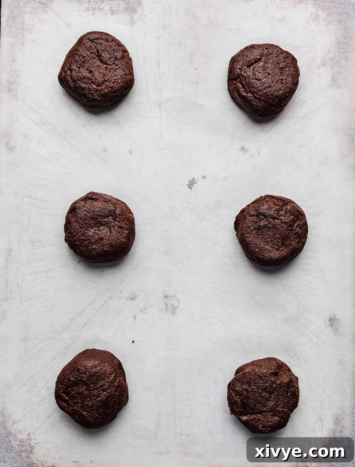 Decadent Mint Brownie Cookie Bliss 5 Six perfectly portioned chocolate cookie dough balls arranged on white parchment paper, ready for baking.