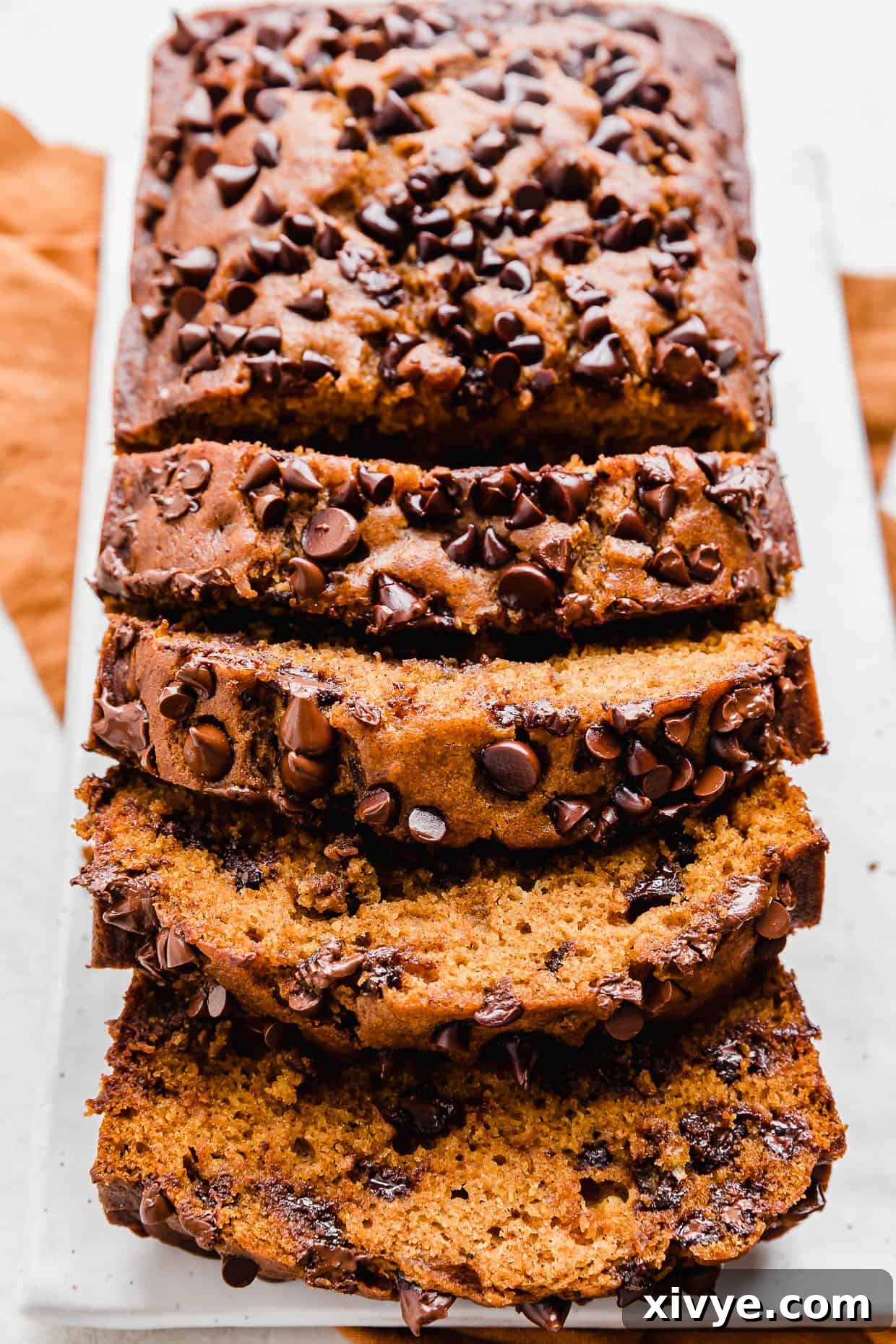 Spiced Pumpkin Chocolate Chip Bread 9 A loaf of Pumpkin Chocolate Chip Bread on a white plate, ready to be sliced and enjoyed.