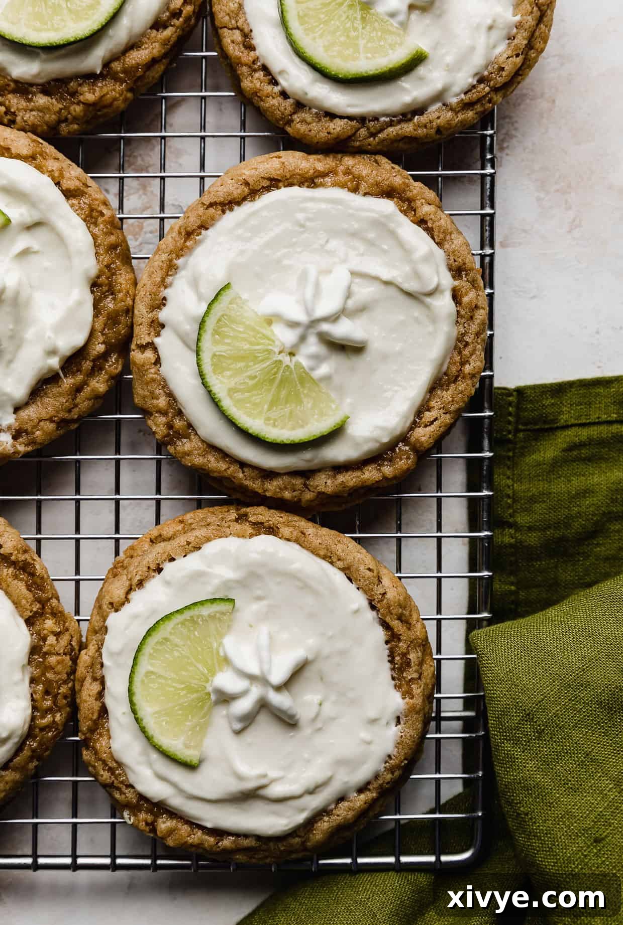 Tangy Key Lime Cookie Delight 11 Copycat Crumbl Key Lime Pie Cookies on a wire cooling rack with a green linen napkin in the bottom right corner.