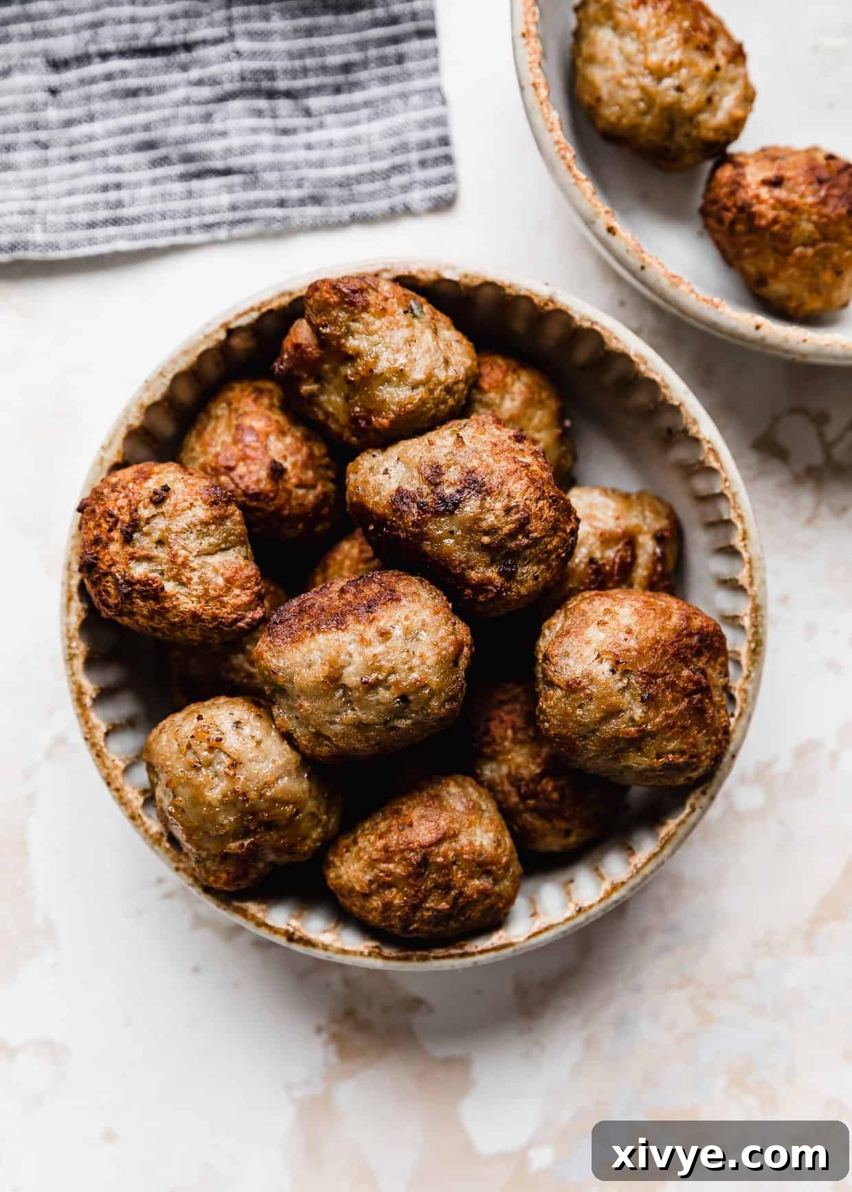 Golden brown and crisped Air Fryer Frozen Meatballs in a ceramic bowl on a white textured background.