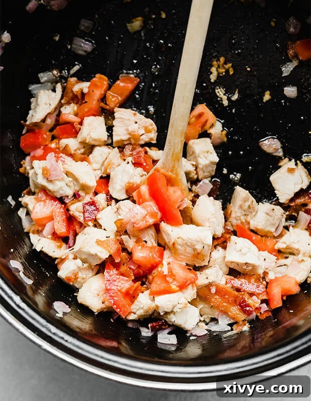 Diced chicken, tomatoes, bacon, and onion in a pot. 