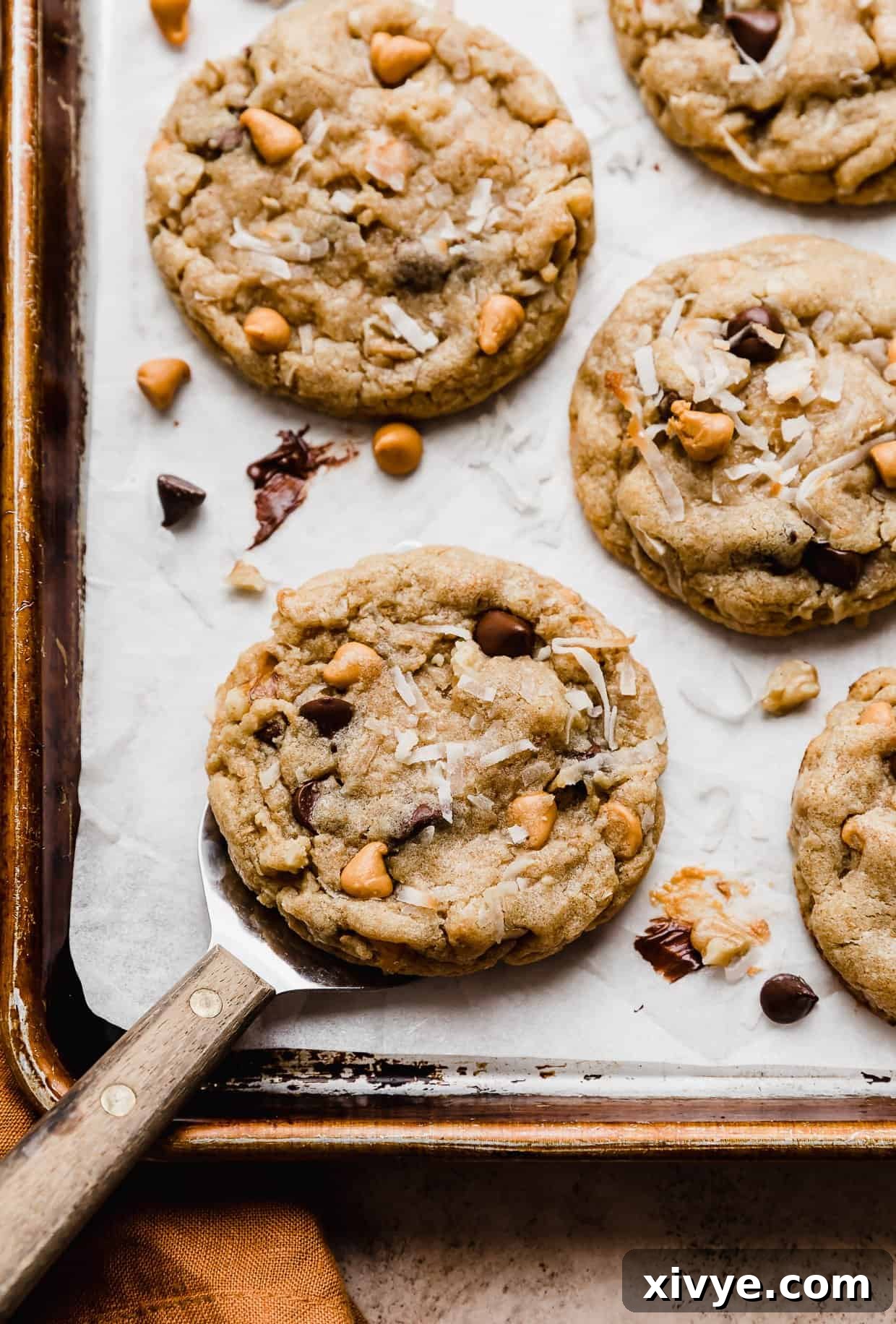 Irresistible Seven-Layer Bars 2 A 7 Layer Bar Cookie on a white parchment lined baking sheet with a wooden spatula under the cookie.