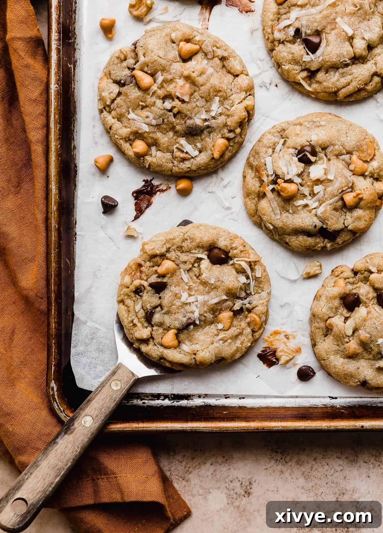 Irresistible Seven-Layer Bars 9 A spatula underneath a 7 Layer Bar Cookie that's on a white parchment lined baking sheet.