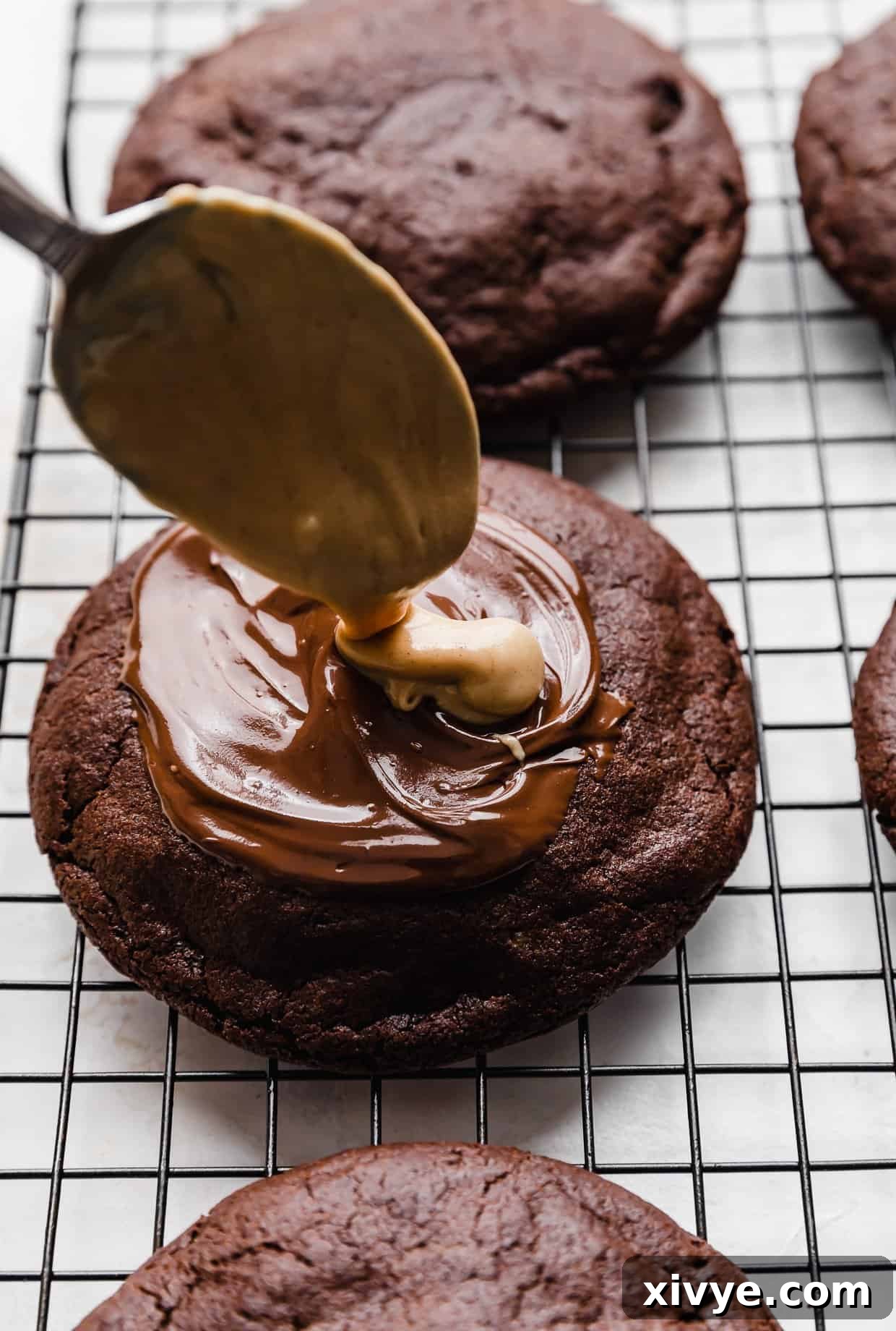 Fudgy Peanut Butter Brownie Cookies 11 A spoon dolloping melted peanut butter overtop a copycat Crumbl Peanut Butter Brownie Cookie.