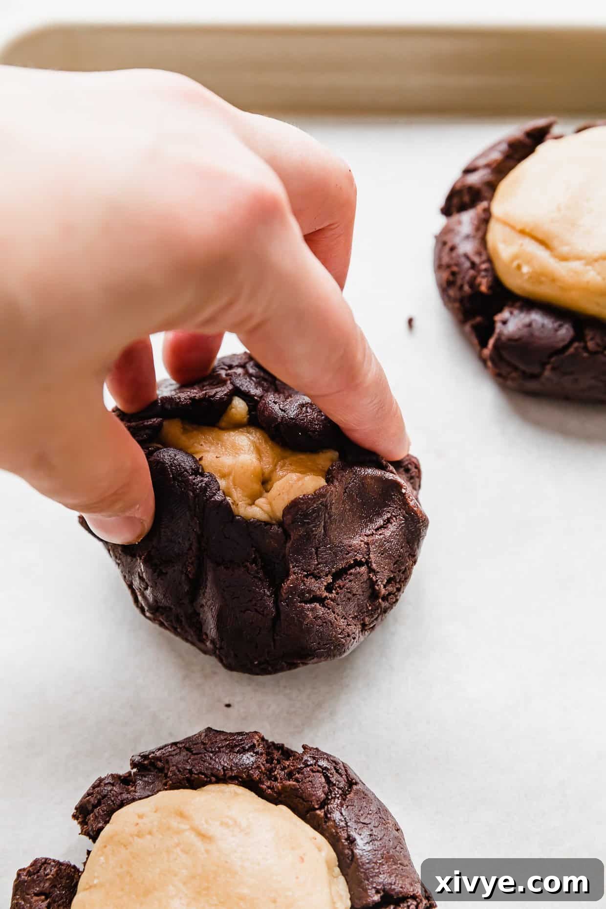 Fudgy Peanut Butter Brownie Cookies 7 A hand pulling the edges of a brownie cookie dough ball overtop of a peanut butter dough ball.