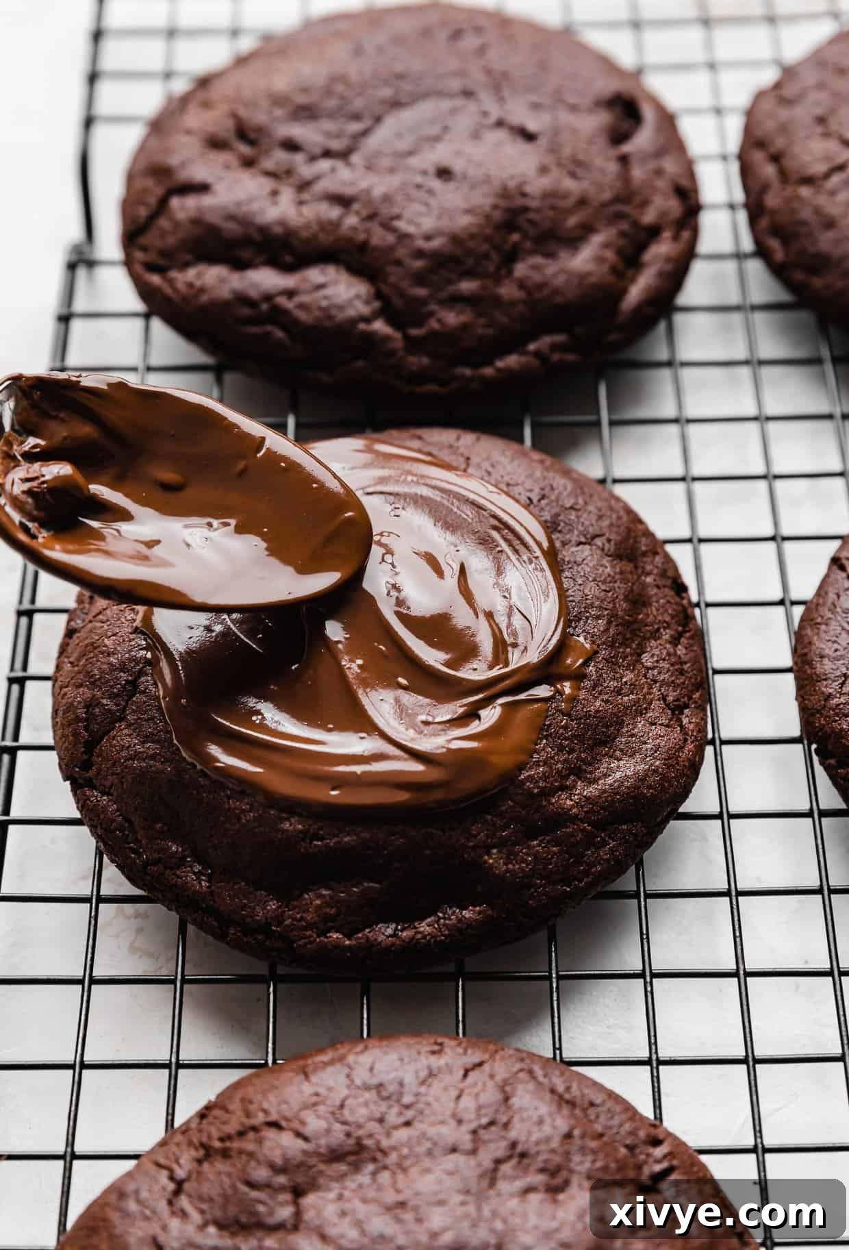 Fudgy Peanut Butter Brownie Cookies 10 A spoon spreading melted chocolate overtop of a Peanut Butter Brownie Cookie on a wire cooling rack.