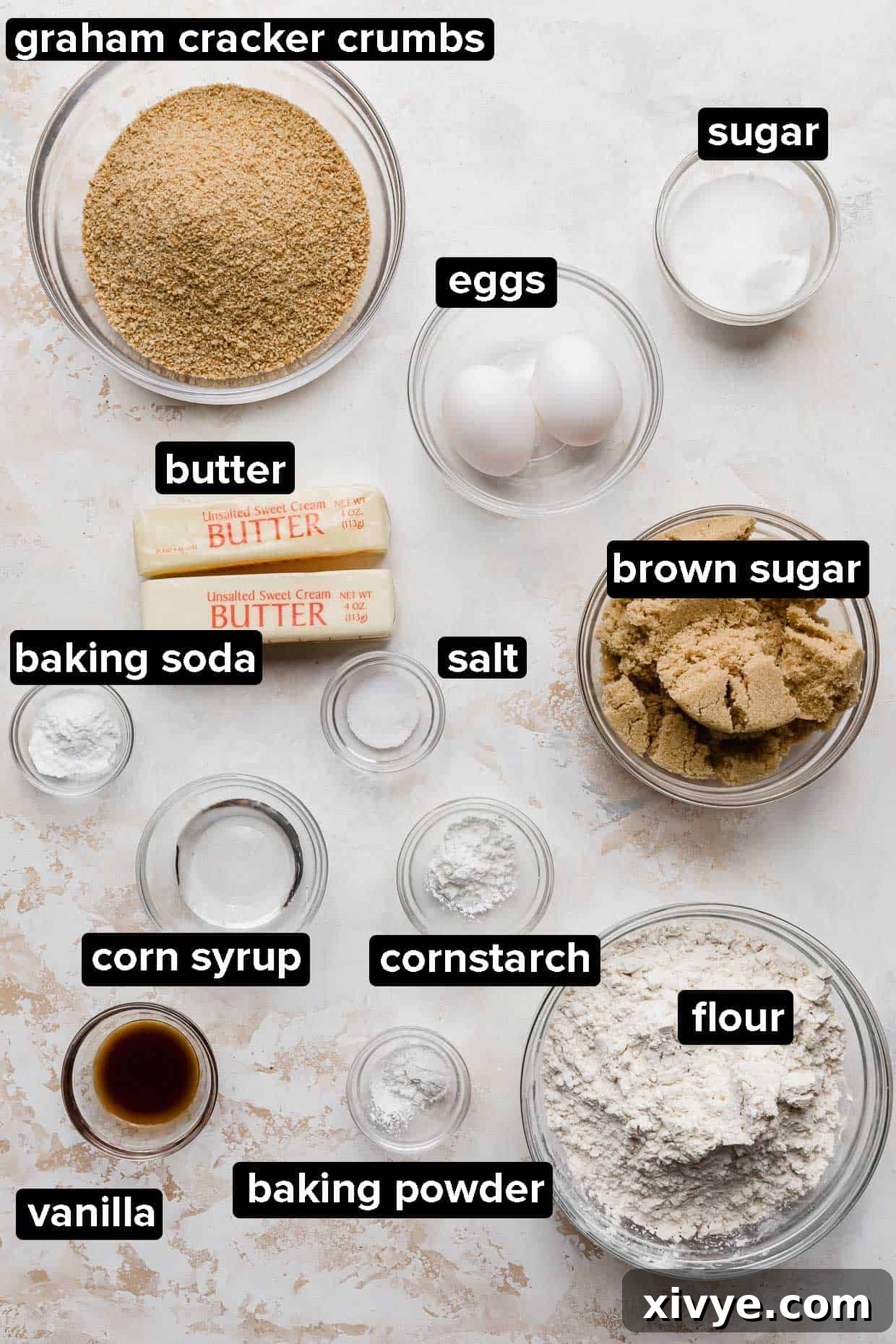 Graham Cracker Cookie ingredients portioned into glass bowls on a white and cream textured background.