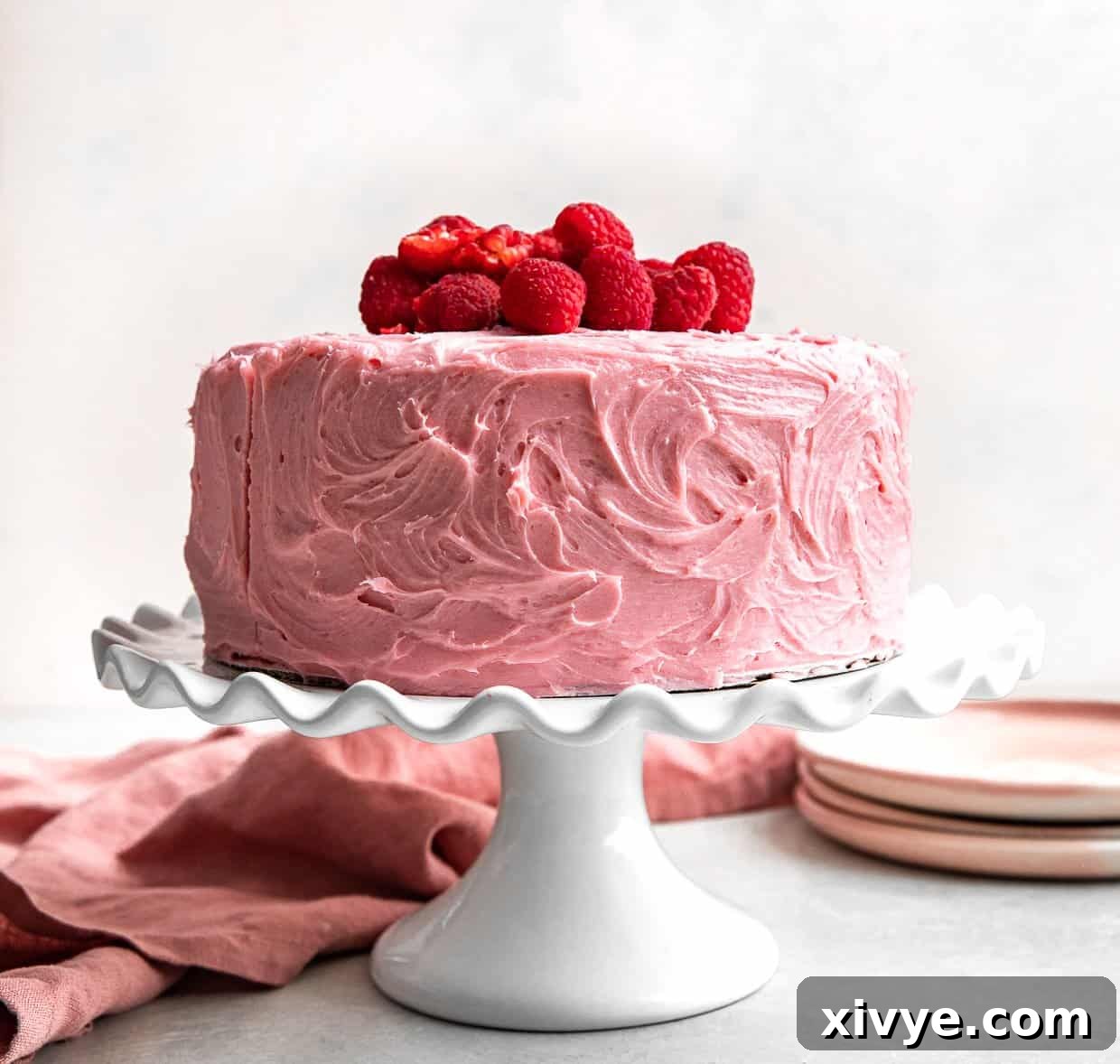 Zesty Lemon Raspberry Delight 11 A stunning two-layer Lemon Raspberry Cake frosted with smooth pink buttercream, presented elegantly on a white cake stand.