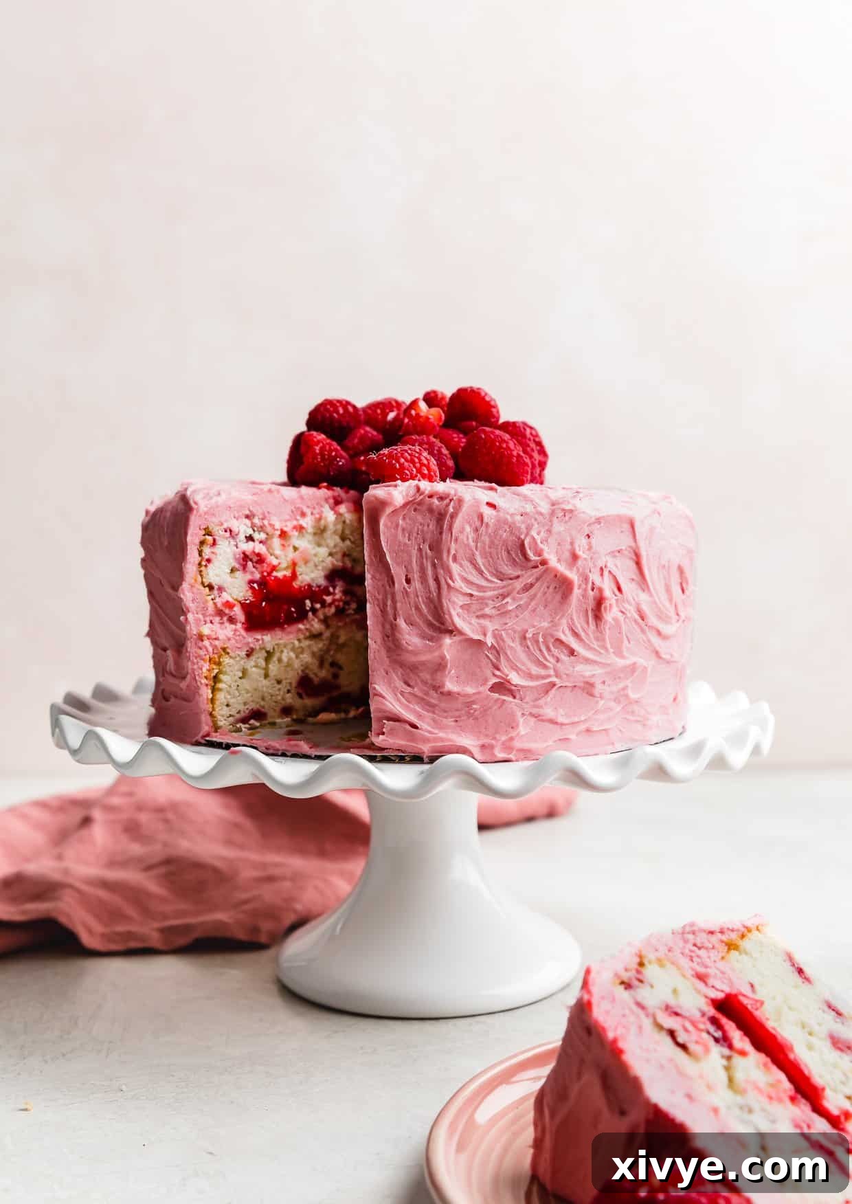 Zesty Lemon Raspberry Delight 12 A beautifully frosted Lemon Raspberry Cake on a white cake stand with one inviting slice removed, showing off the interior.