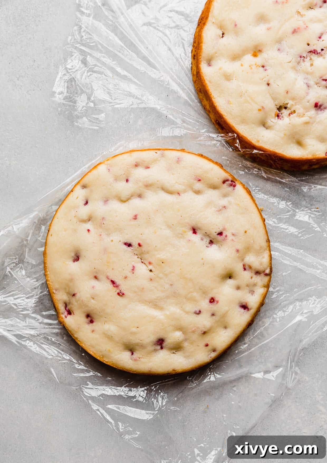 Zesty Lemon Raspberry Delight 4 A perfectly baked, round Lemon Raspberry cake layer resting on a piece of plastic wrap, ready for cooling.