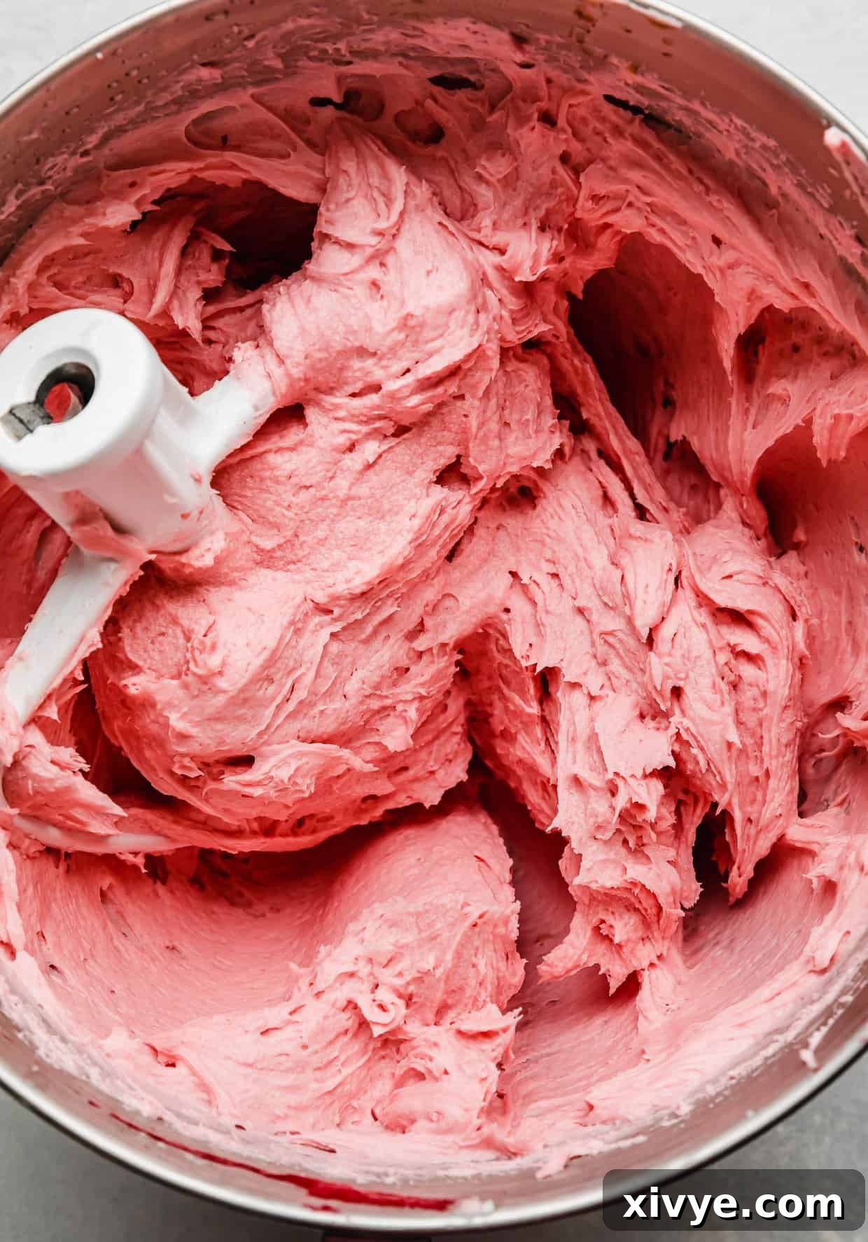 Zesty Lemon Raspberry Delight 6 A close-up of vibrant pink raspberry buttercream in a metal mixing bowl, showcasing its smooth, creamy texture.