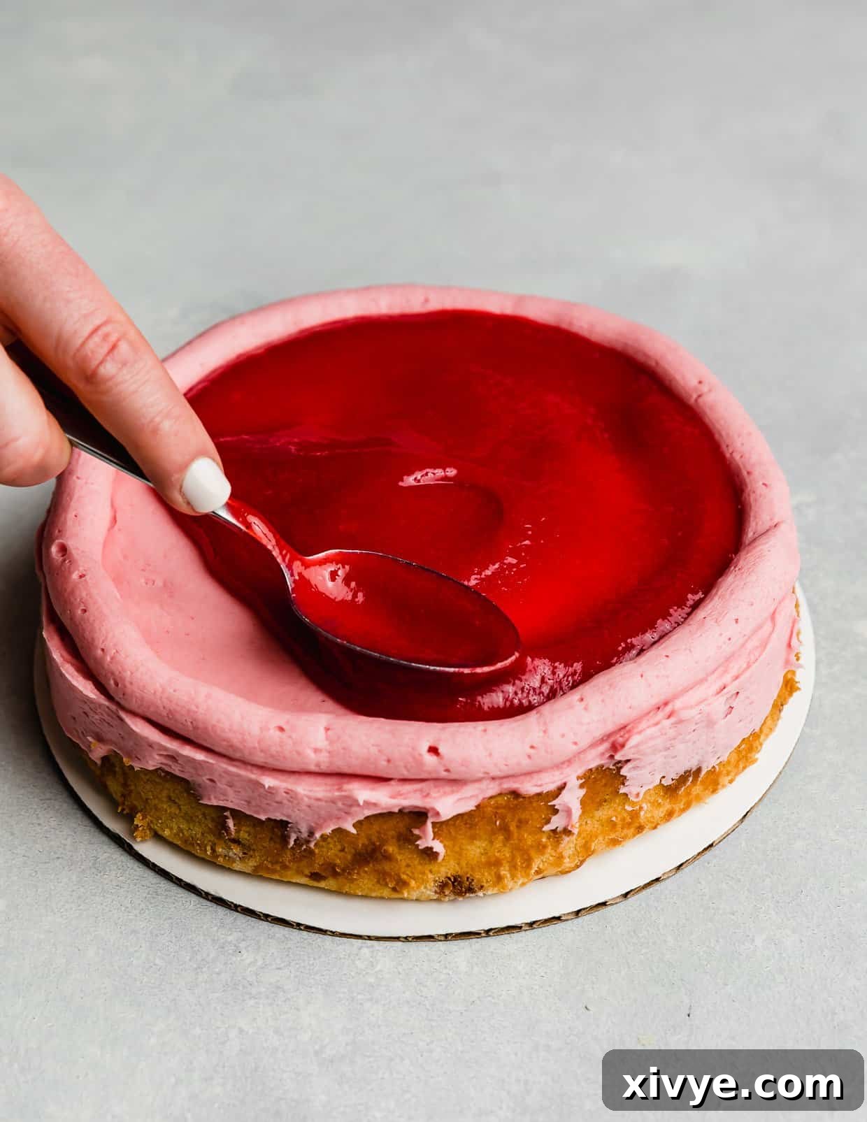 Zesty Lemon Raspberry Delight 8 A spoon meticulously spreading a vibrant raspberry filling over a round cake layer, contained by a piped buttercream dam.