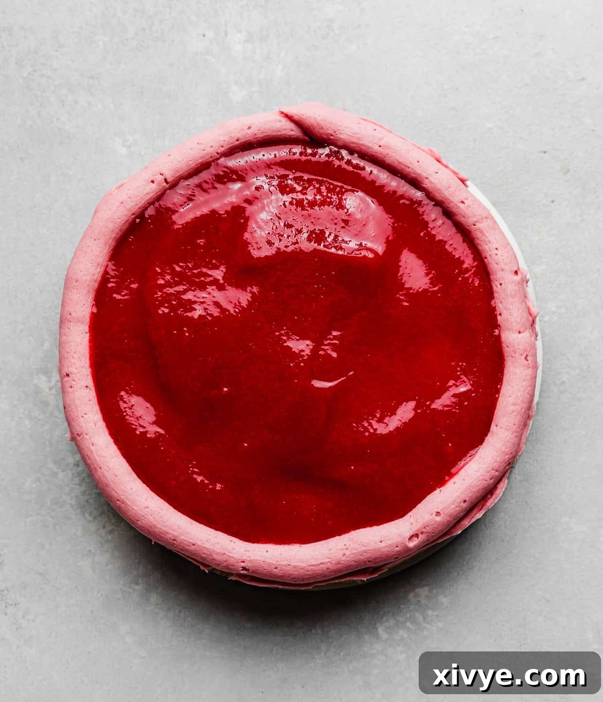 Zesty Lemon Raspberry Delight 9 An overhead view of a glistening raspberry sauce spread evenly over a round cake layer, prepared for the next tier.