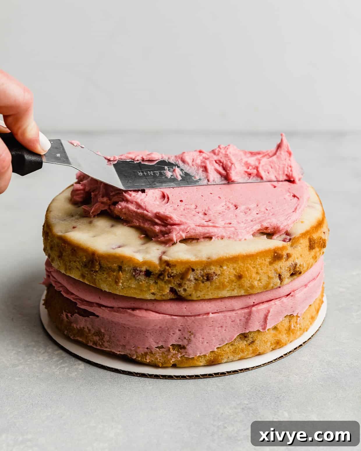 Zesty Lemon Raspberry Delight 10 A spatula smoothly spreading a pink raspberry frosting over a two-layer cake, creating a perfect crumb coat.