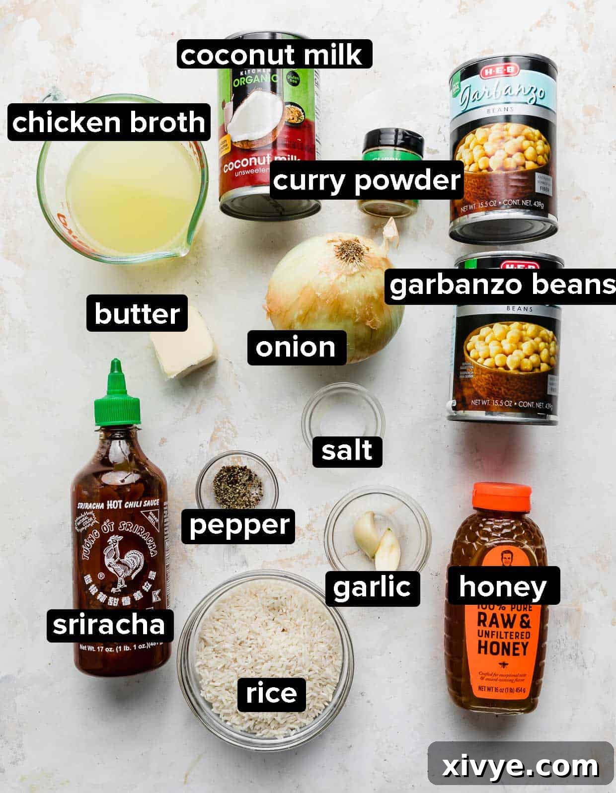 An array of fresh ingredients including canned chickpeas, coconut milk, onions, garlic, and spices laid out for making chickpea curry.