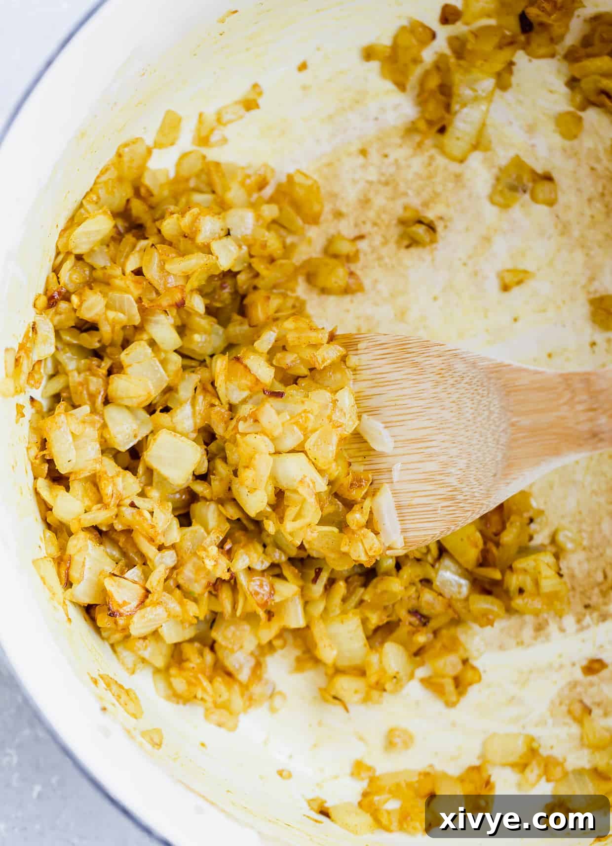 Curry powder being stirred into sautéed onions and garlic in a pan, releasing its fragrant aroma.