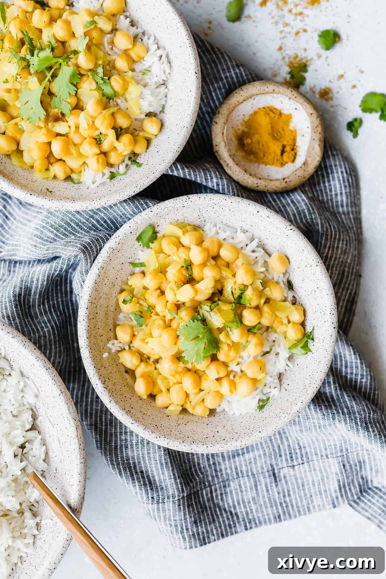 Three bowls of fluffy rice, two generously topped with vibrant chickpea curry and fresh cilantro garnish, inviting to a shared meal.