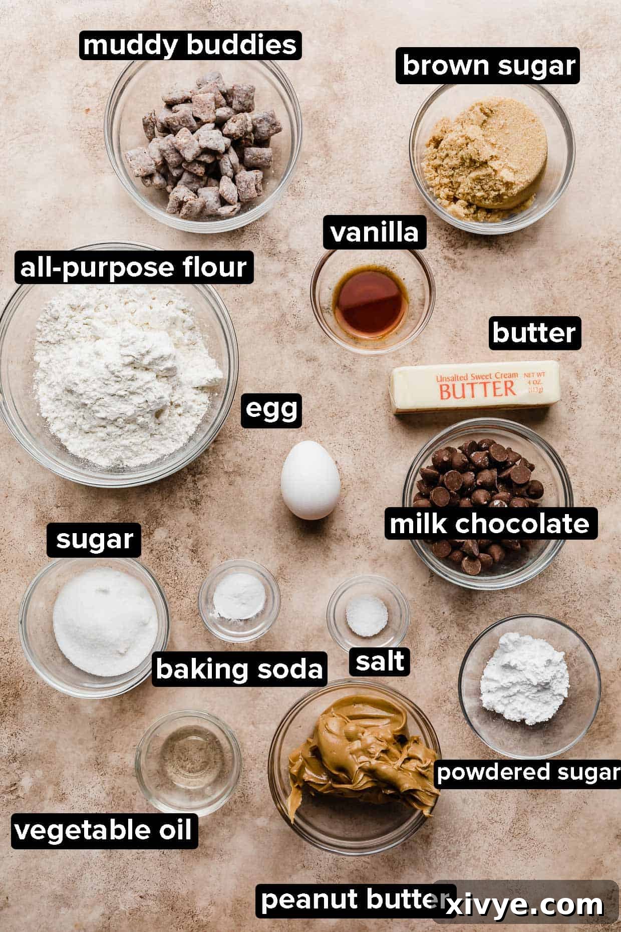 Crumbl Muddy Buddy Cookie ingredients portioned into glass bowls on a tan textured background, including butter, peanut butter, sugar, flour, and chocolate.