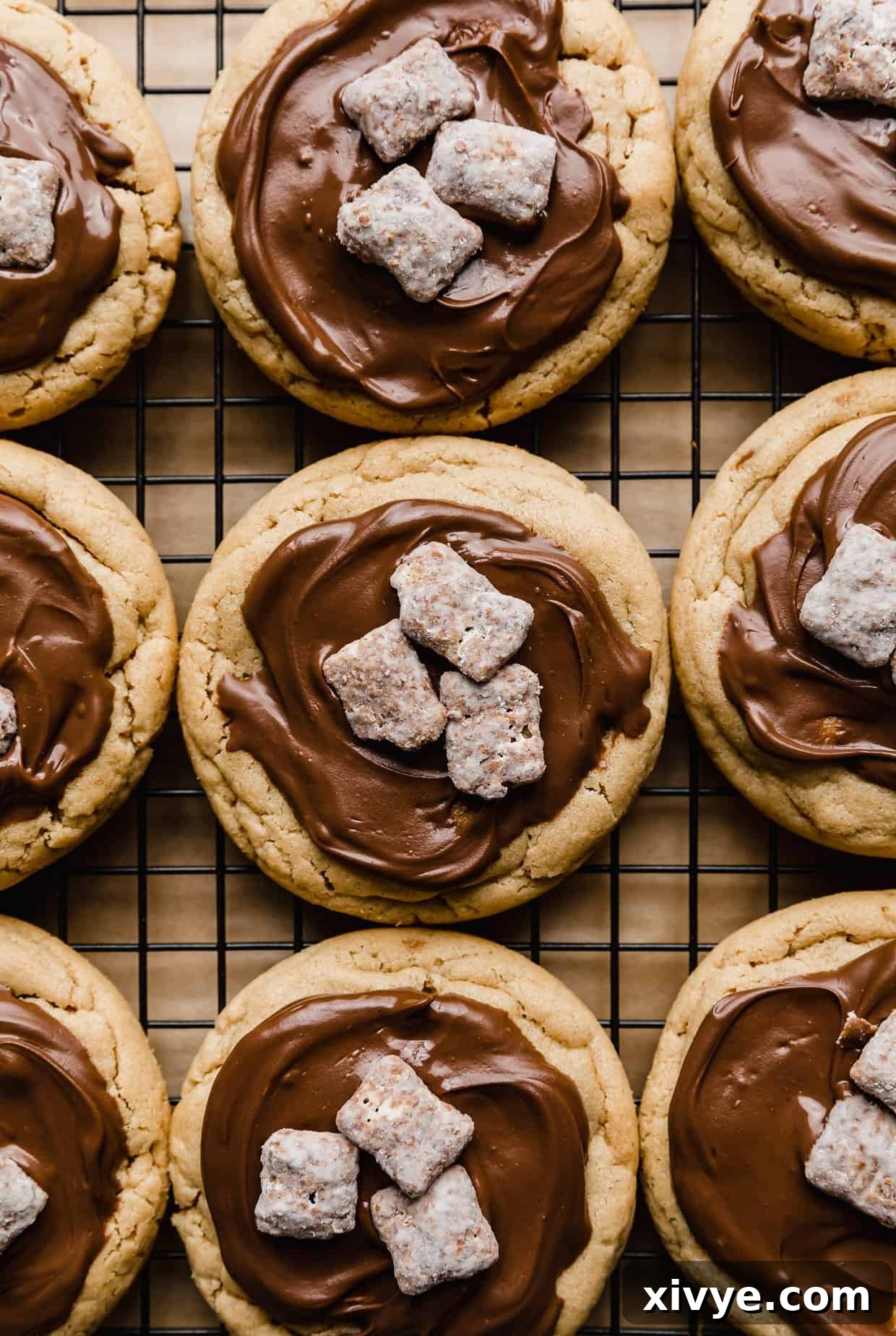 Crumbl Muddy Buddy Cookies topped with melted chocolate and three muddy buddy pieces, finished with a delicate dusting of powdered sugar.