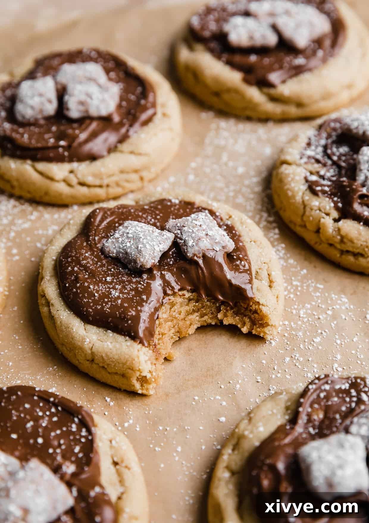 A Crumbl Muddy Buddy Cookie with a bite taken out, resting on a tan parchment paper, revealing its soft interior.