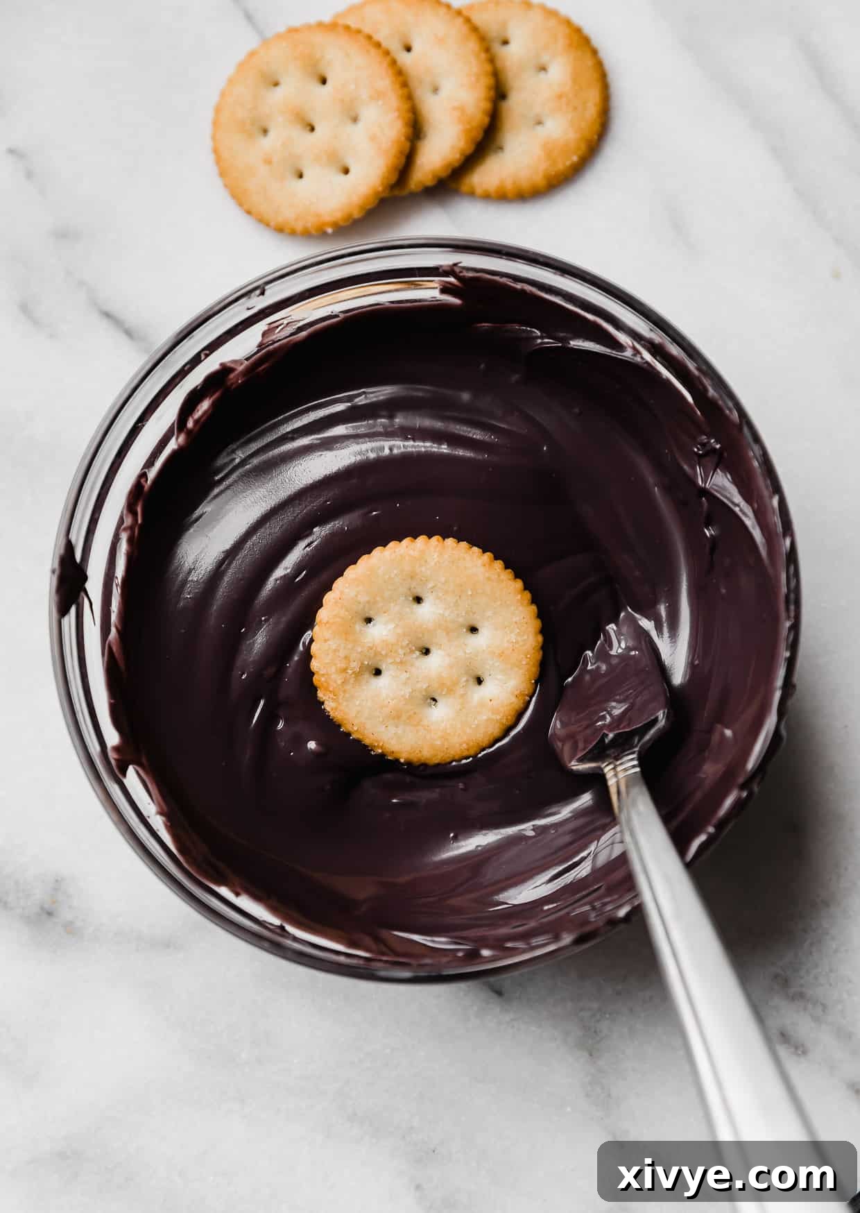 A ritz cracker in a bowl filled with black melted chocolate.