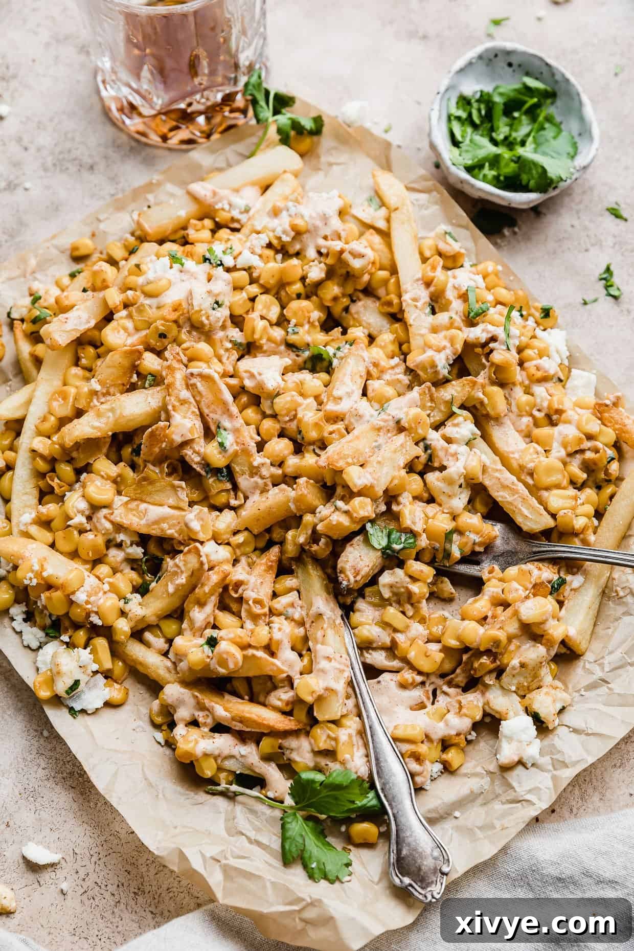 Golden Corn Sticks 9 Delicious Corn Fries piled high, topped with a vibrant Mexican Street Corn mixture, crumbled cheese, and fresh cilantro, served on parchment paper.