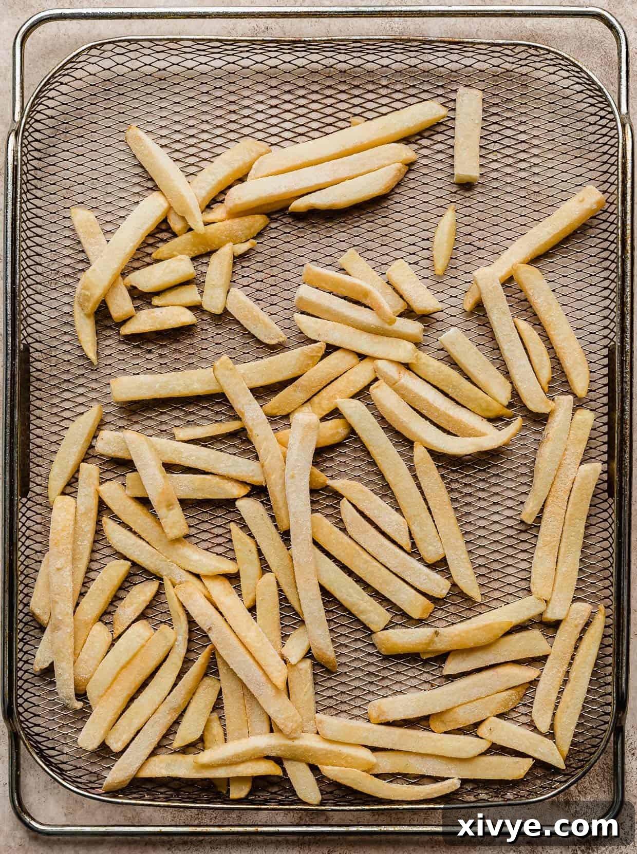 Frozen French fries on a metal air fryer basket.