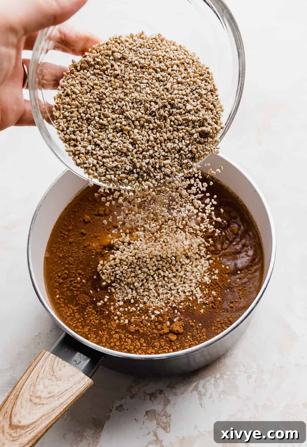 Spiced Pumpkin Steel Cut Oats 4 A hand pouring in raw steel cut oats into a saucepan.