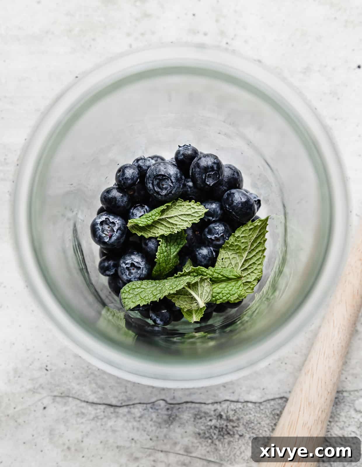 A glass jar with a handful of fresh blueberries and mint leaves in the bottom, in preparation to make a blueberry mocktail.