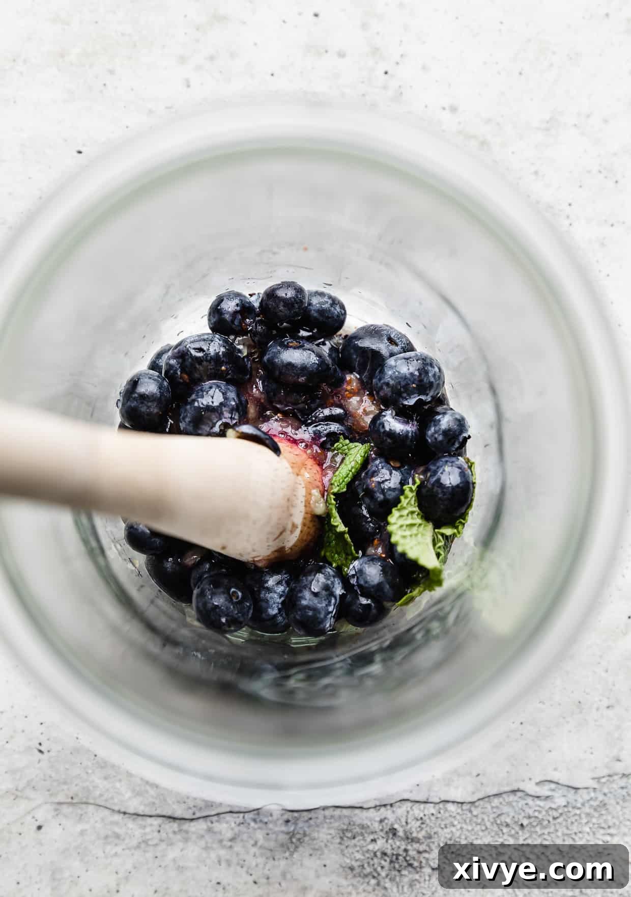 A wood muddle pressing down on blueberries and mint leaves, gently extracting their flavors.