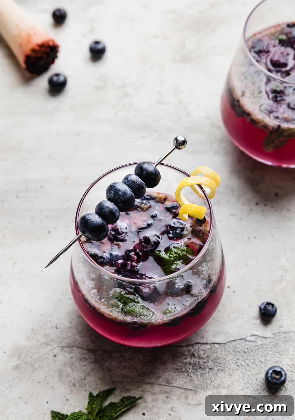 A glass cup filled with blueberry mocktail drink, garnished with mint and blueberries.