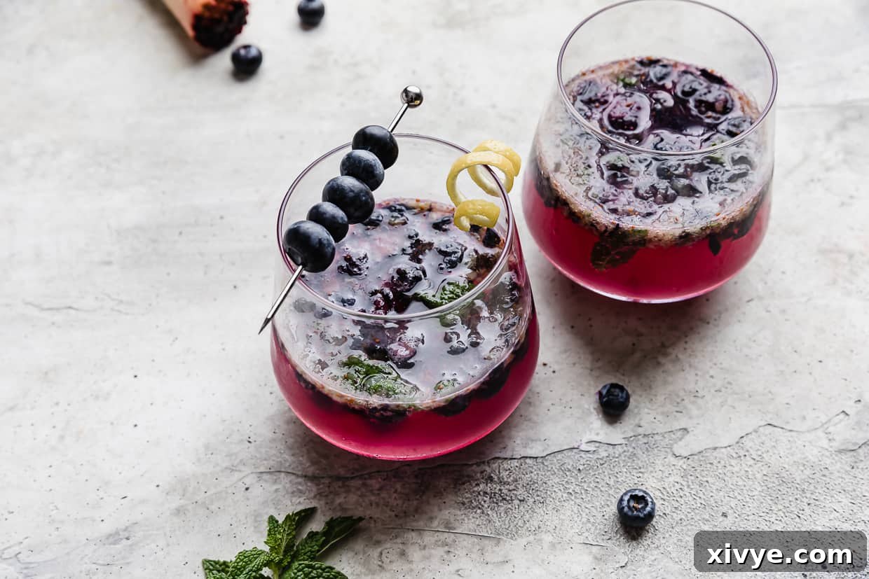 A glass cup on a gray background filled with blueberry mojito mocktail recipe, with a focus on the drink's vibrant color.