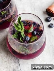 A glass cup on a gray background filled with a blueberry mojito mocktail.