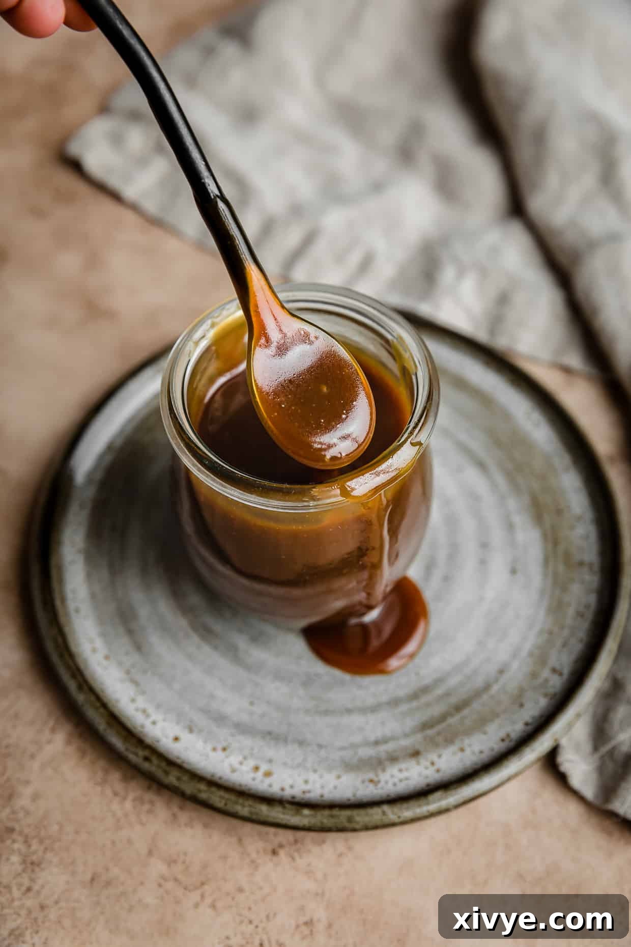 A spoon with homemade Salted Butterscotch Sauce on it, ready to be drizzled.