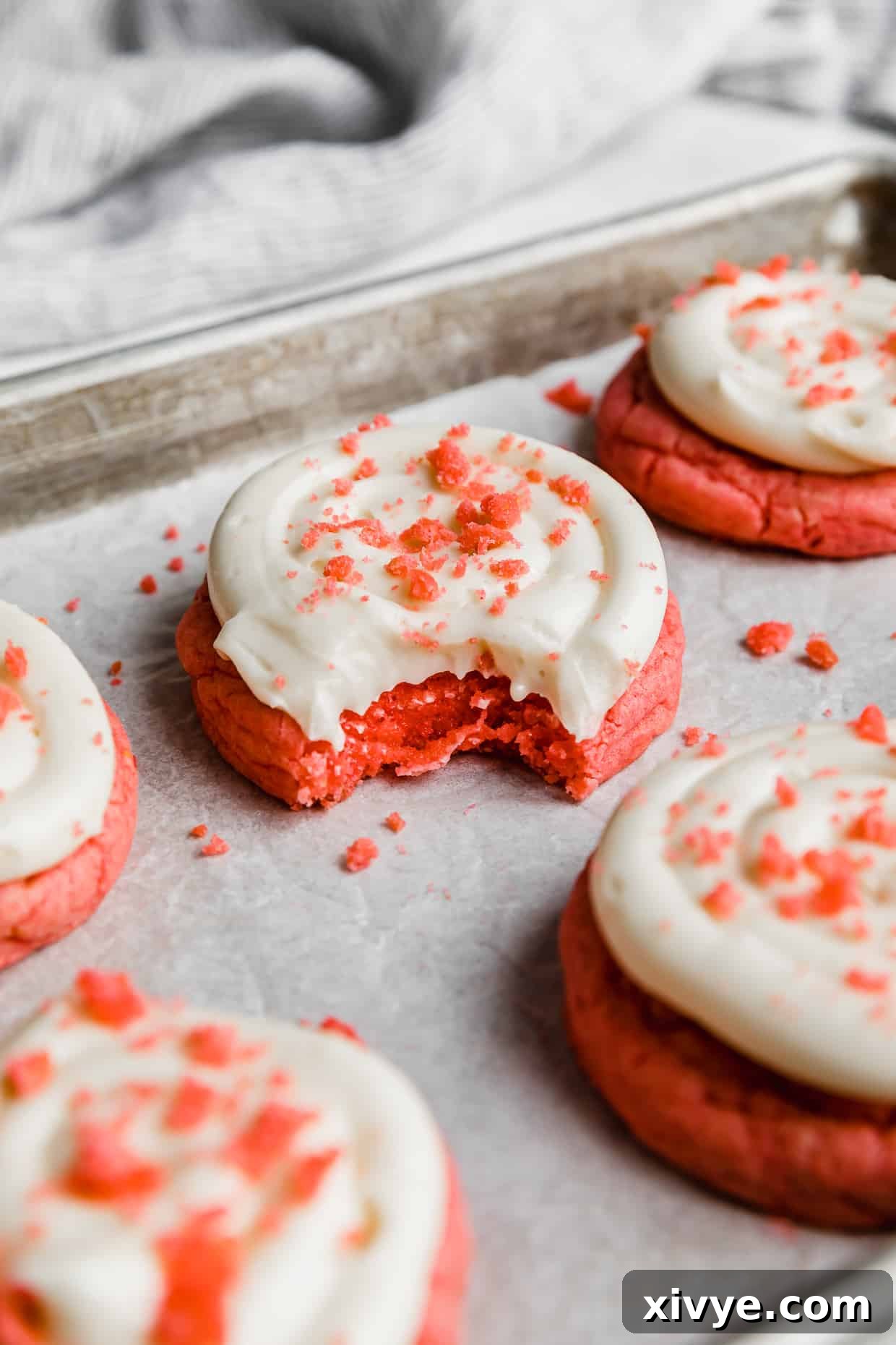 A Crumbl Pink Velvet Cookie topped with cream cheese frosting with a bite taken out of the cookie.