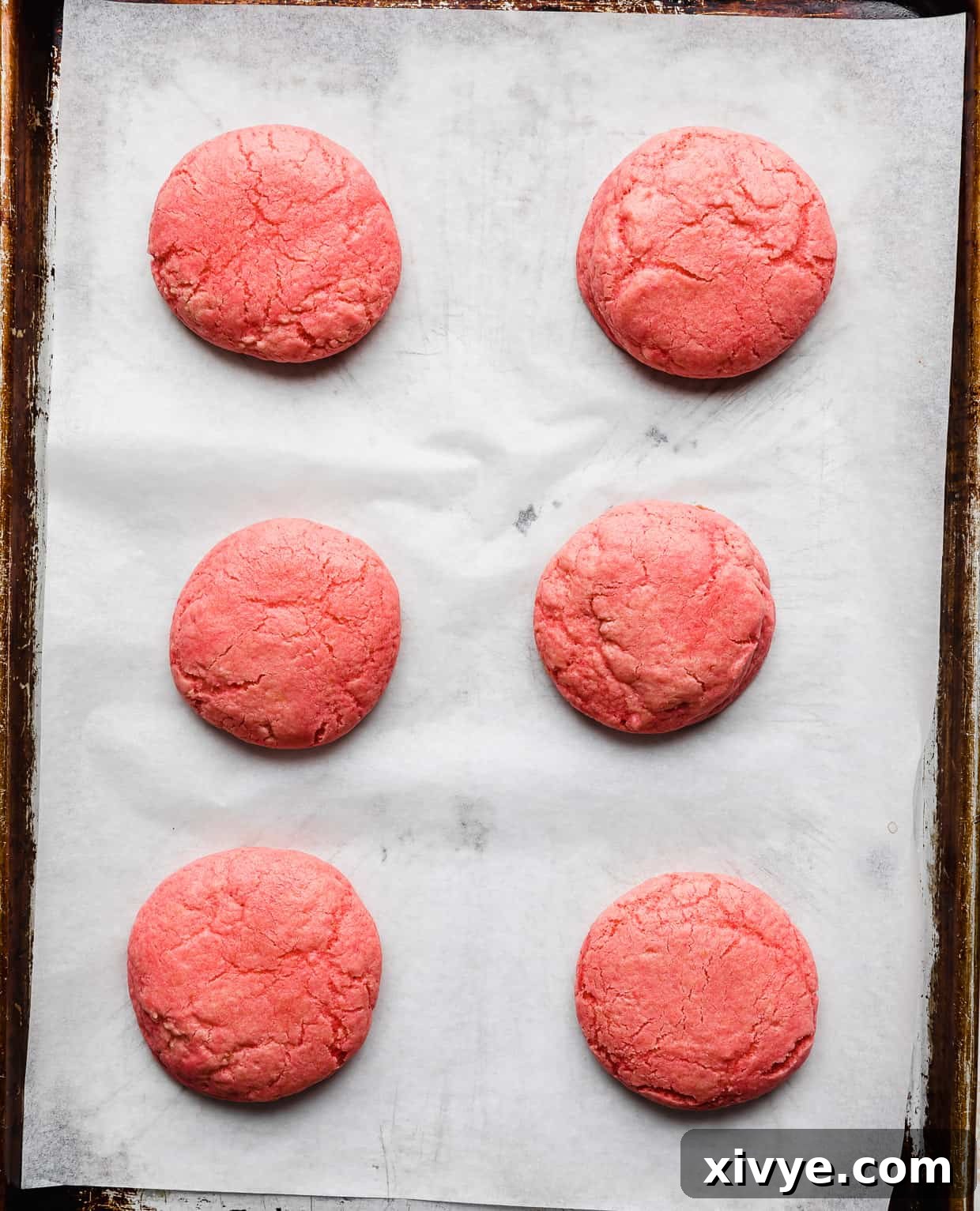 Six pink velvet cookies on a baking sheet.