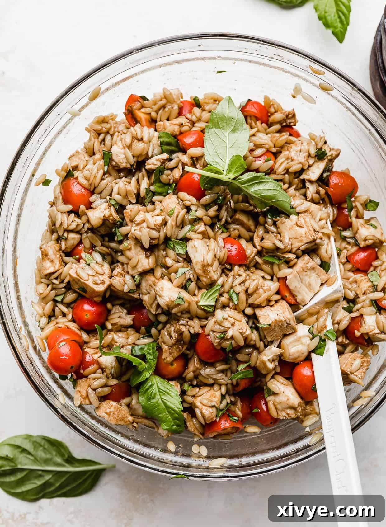 Mediterranean Orzo Delight 17 A vibrant Caprese Orzo Salad in a clear glass bowl, garnished with fresh basil leaves, showcasing its fresh ingredients.