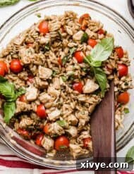 A Caprese Orzo Salad with fresh basil, chicken, tomatoes, and orzo in a glass bowl on a white background.