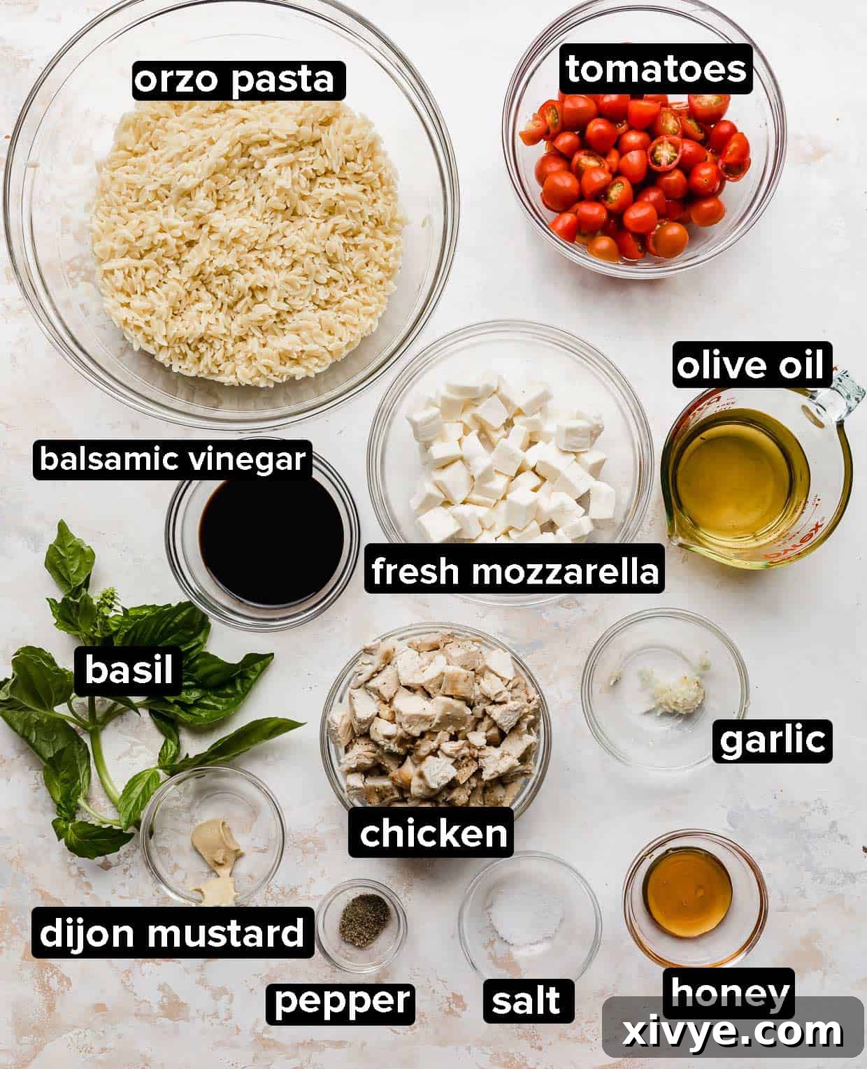 A selection of fresh ingredients for Caprese Orzo Salad, including tomatoes, mozzarella, basil, and a bottle of balsamic vinegar, artfully arranged on a white background.