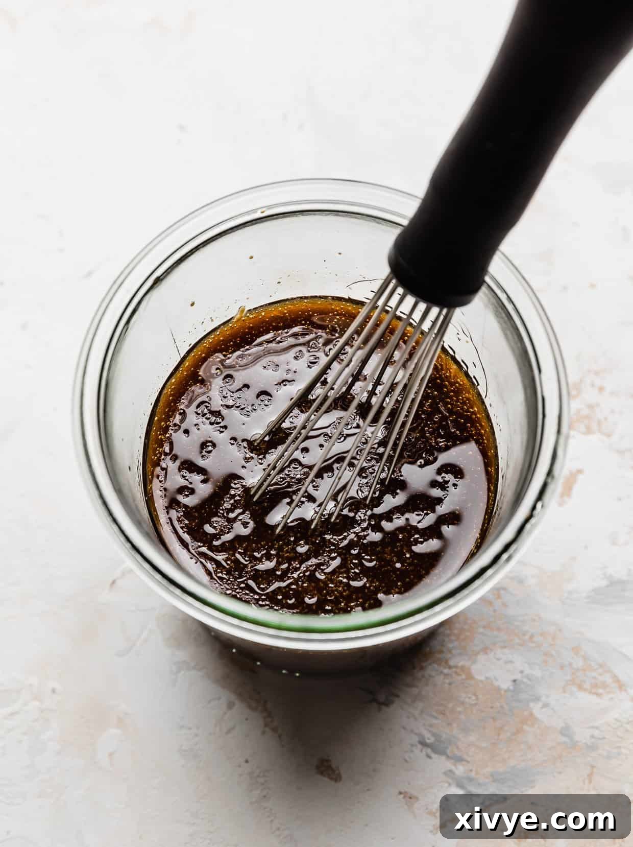 A clear glass jar filled with a freshly prepared balsamic vinaigrette, showing the emulsion of oil and vinegar, on a pristine white background.