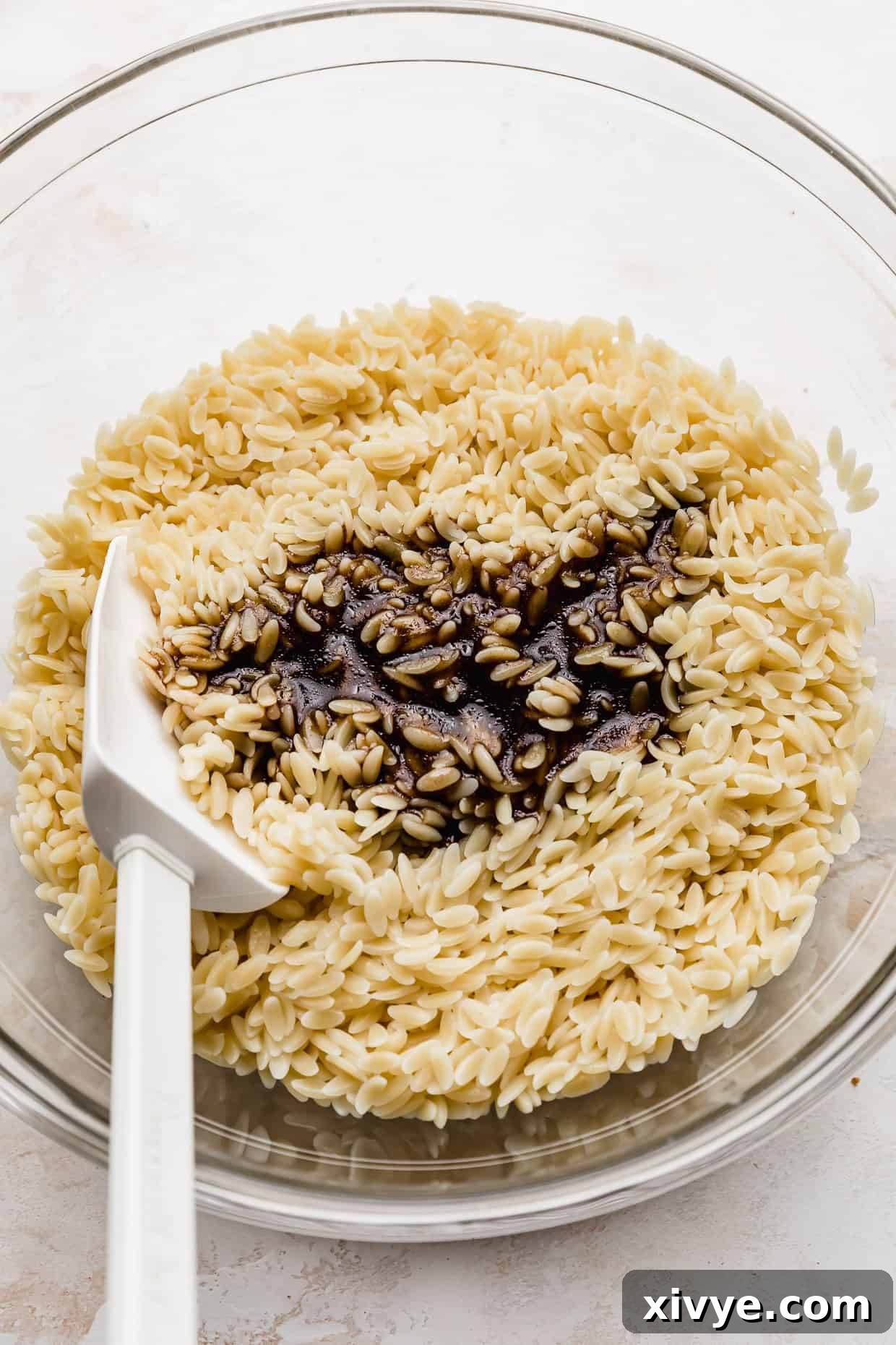 Freshly cooked orzo pasta in a bowl, being drizzled with rich balsamic dressing, ready for tossing.