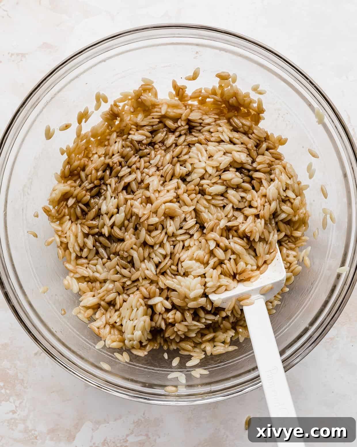 Orzo pasta thoroughly coated in a glossy balsamic dressing, signifying the first step of flavor infusion for the Caprese salad.