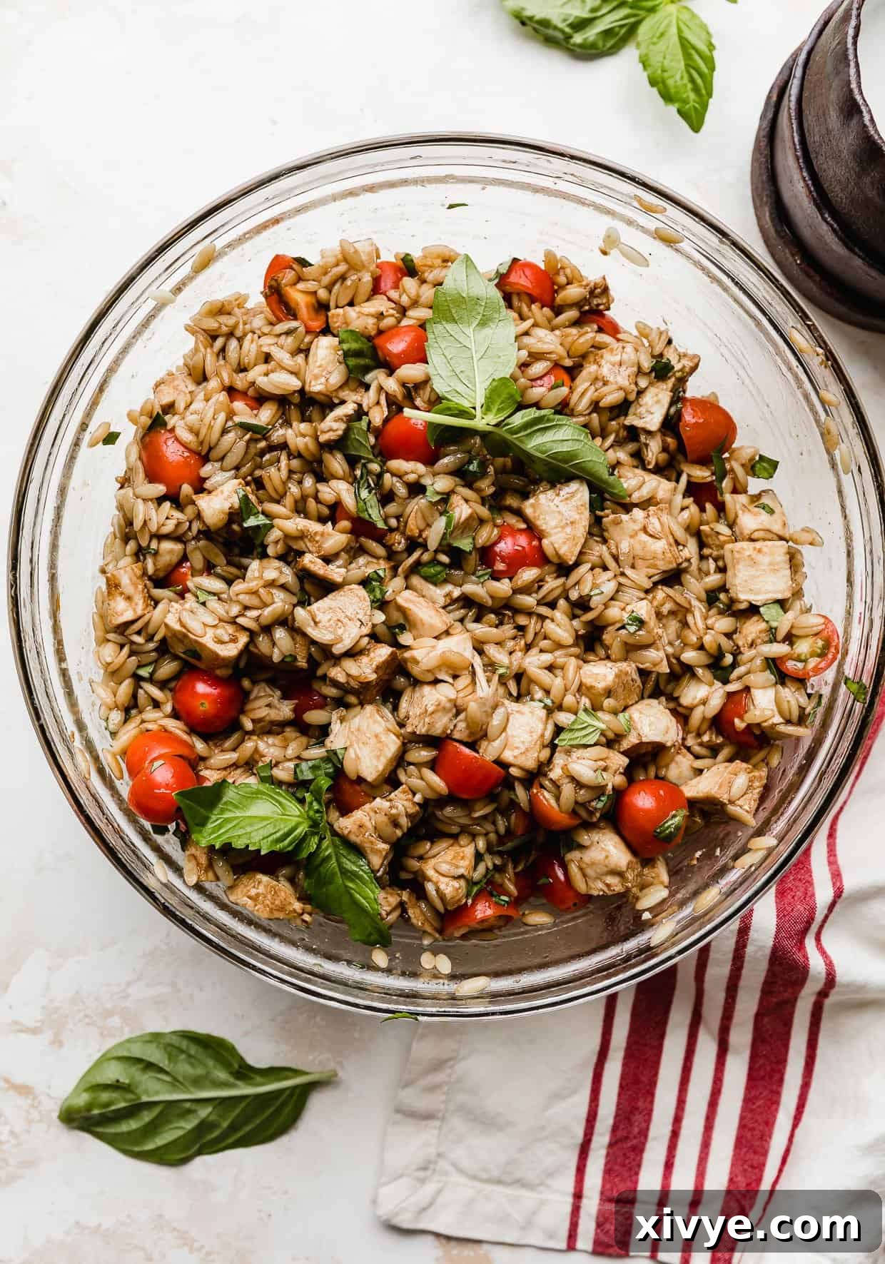 A stunning close-up of a Chicken Caprese Orzo Salad in a glass bowl, showcasing the rich balsamic dressing coating the fresh ingredients, ready to be served.